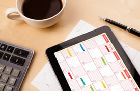 Workplace with tablet pc showing calendar and a cup of coffee on a wooden work table close-up.jpeg